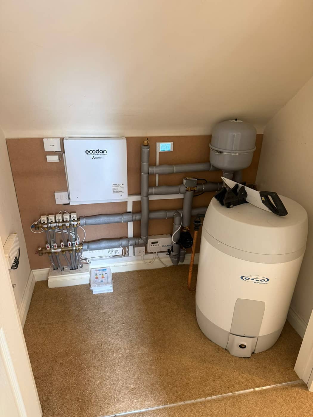 A tidy under-eaves cupboard with a hot water cylinder, underfloor heating manifold and control panel