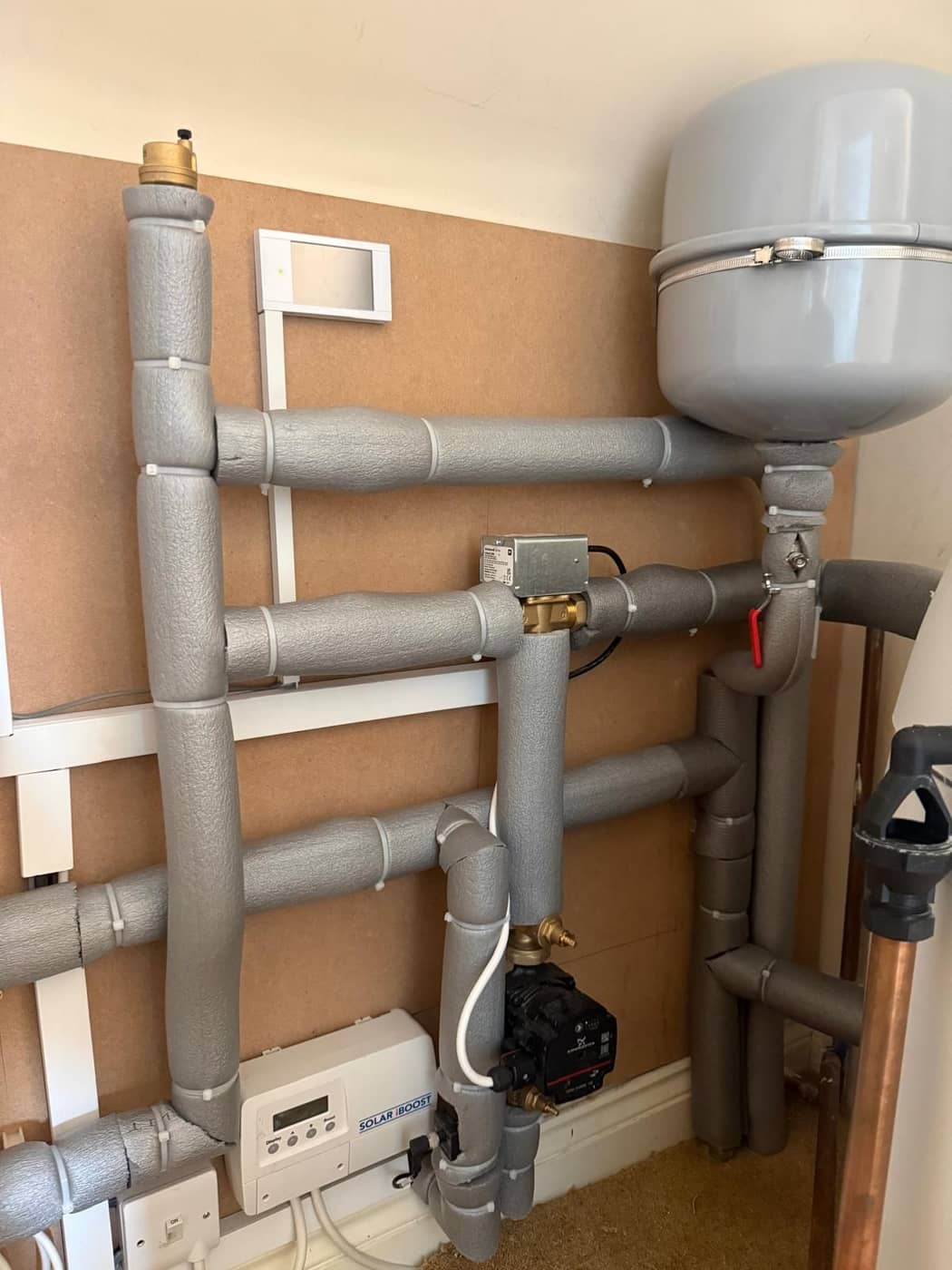 Grey insulated pipework and a circulating pump neatly fixed to a boarded wall