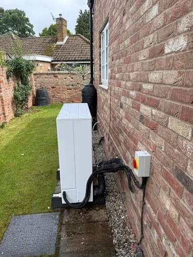 A white heat pump in a gravel side passage beside a brick house