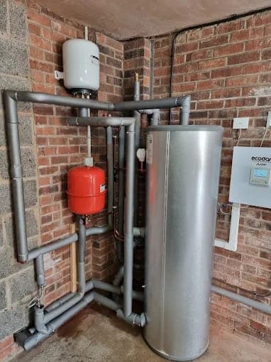 A heat pump cylinder with insulated pipework and controller in the corner of a brick room