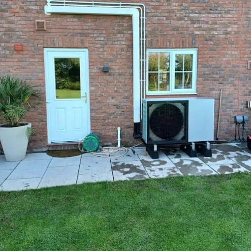 A heat pump on the back wall of a house beside a white door and lawn