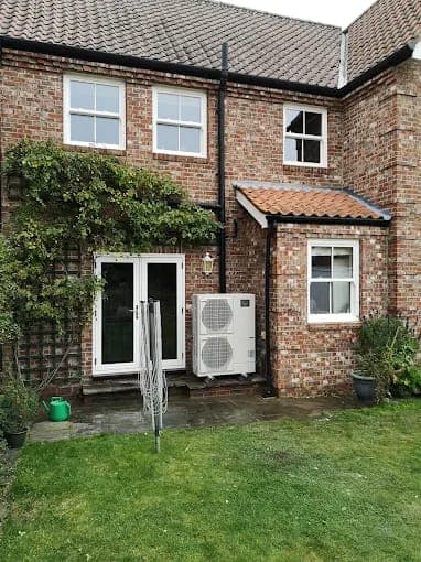 The back of a brick house with a heat pump beside the patio doors