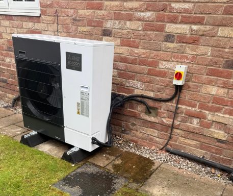 5KW - R32 Heat Pump Air source heat pump mounted on a brick wall, with a power disconnect switch nearby.